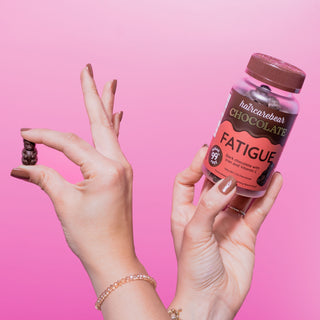 A hand holding a bottle of Haircarebear Fatigue Chocolate gummies, with another hand presenting one gummy