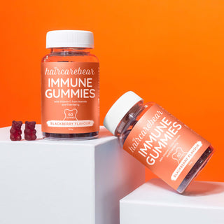 Two packs of Haircarebear Immune Gummies are placed on two levels of white platforms, one angled towards the other, with two gummies.